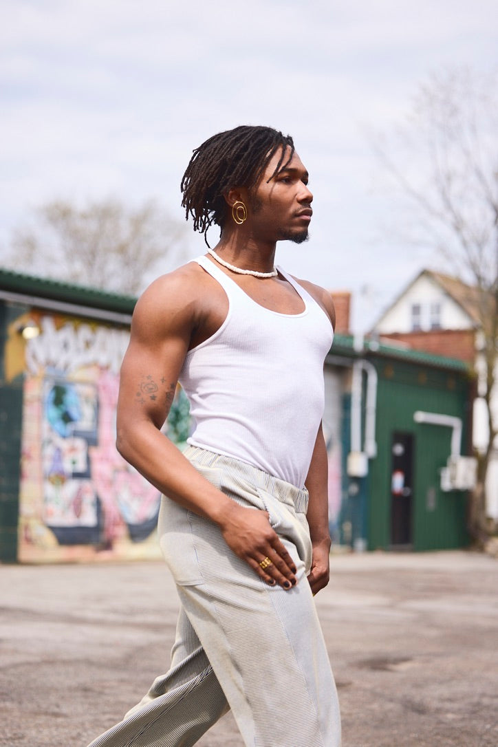 Person wearing a white tank top and light-colored pants outdoors with a mural in the background.