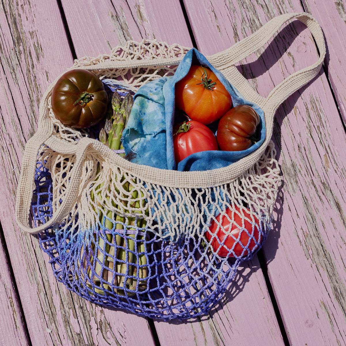 Mesh produce bag filled with tomatoes and other vegetables on a wooden surface