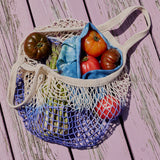 Mesh produce bag filled with tomatoes and other vegetables on a wooden surface