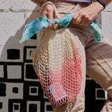 Person holding a colorful mesh bag against a geometric-patterned wall.