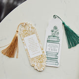 A styled flat-lay of two decorative bookmarks on a white marble surface next to notebooks. The bookmarks include one with a gold foil pattern and a gold tassel, and another with a green tassel.