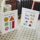 Two white framed educational art prints titled 'Shapes of Buffalo' and 'Colors of Buffalo' displayed on a green and white hexagonal tile floor in a rustic room setting.