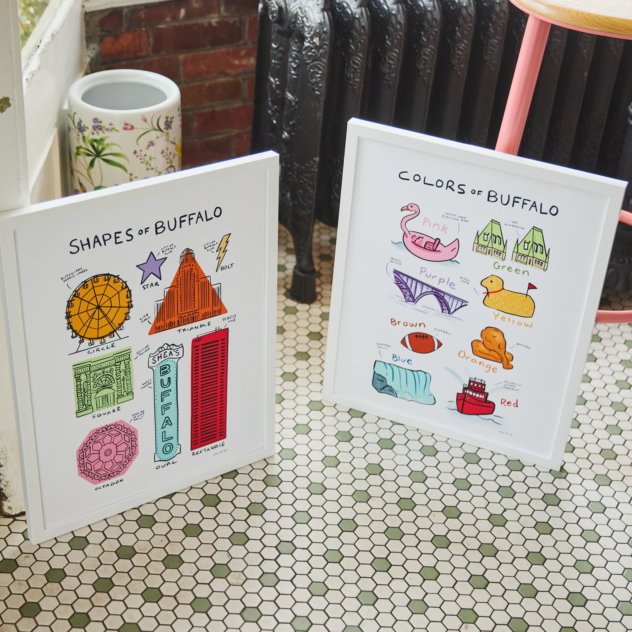 Two white framed educational art prints titled 'Shapes of Buffalo' and 'Colors of Buffalo' displayed on a green and white hexagonal tile floor in a rustic room setting.