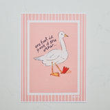 A square art print featuring a white goose with one foot in front of the other, set against a pink background with a striped border. Handwritten text reads 'one foot in front of the other.