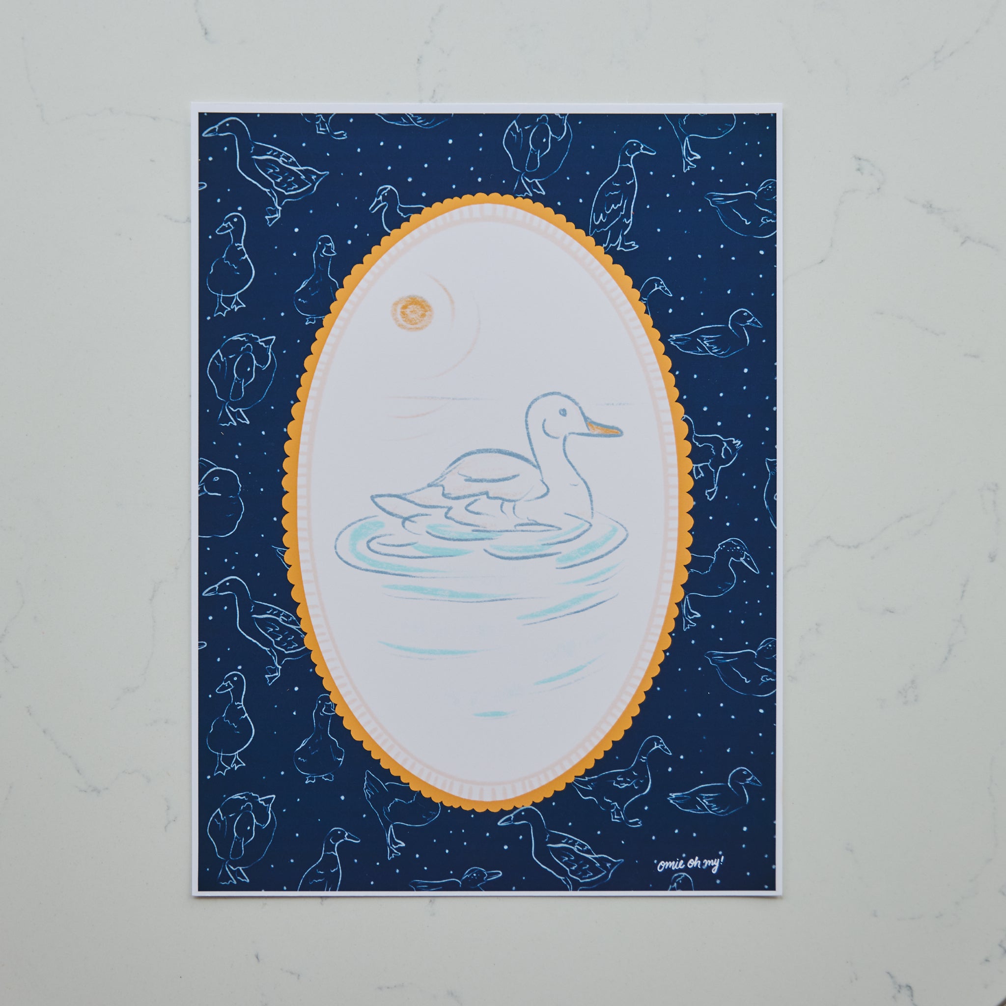 A square art print featuring a white duck swimming in a light blue pond, framed by a scalloped gold oval border on a dark navy blue background with starry speckles and faint duck silhouettes. The print is photographed flat against a light gray marble surface.