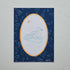 A square art print featuring a white duck swimming in a light blue pond, framed by a scalloped gold oval border on a dark navy blue background with starry speckles and faint duck silhouettes. The print is photographed flat against a light gray marble surface.
