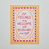 A square art print with a colorful quote reading 'All Feelings are Welcome, all Behaviors are not'. The print features a red and white checkered border, a yellow oval frame, and a yellow and white striped background, displayed on a light gray marble surface.