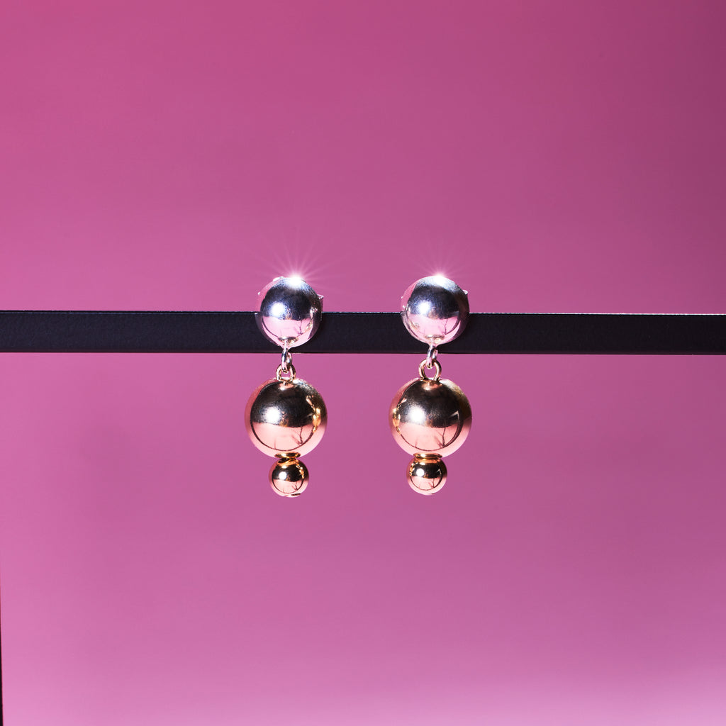 Two of Peg's Hardware's Sol earrings, hanging from a black metal frame.