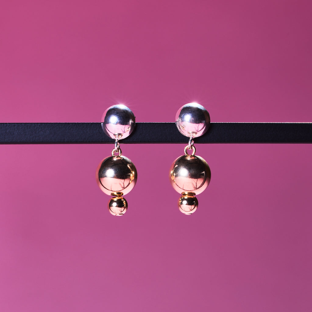 Two of Peg's Hardware's Sol earrings, hanging from a black metal frame. 