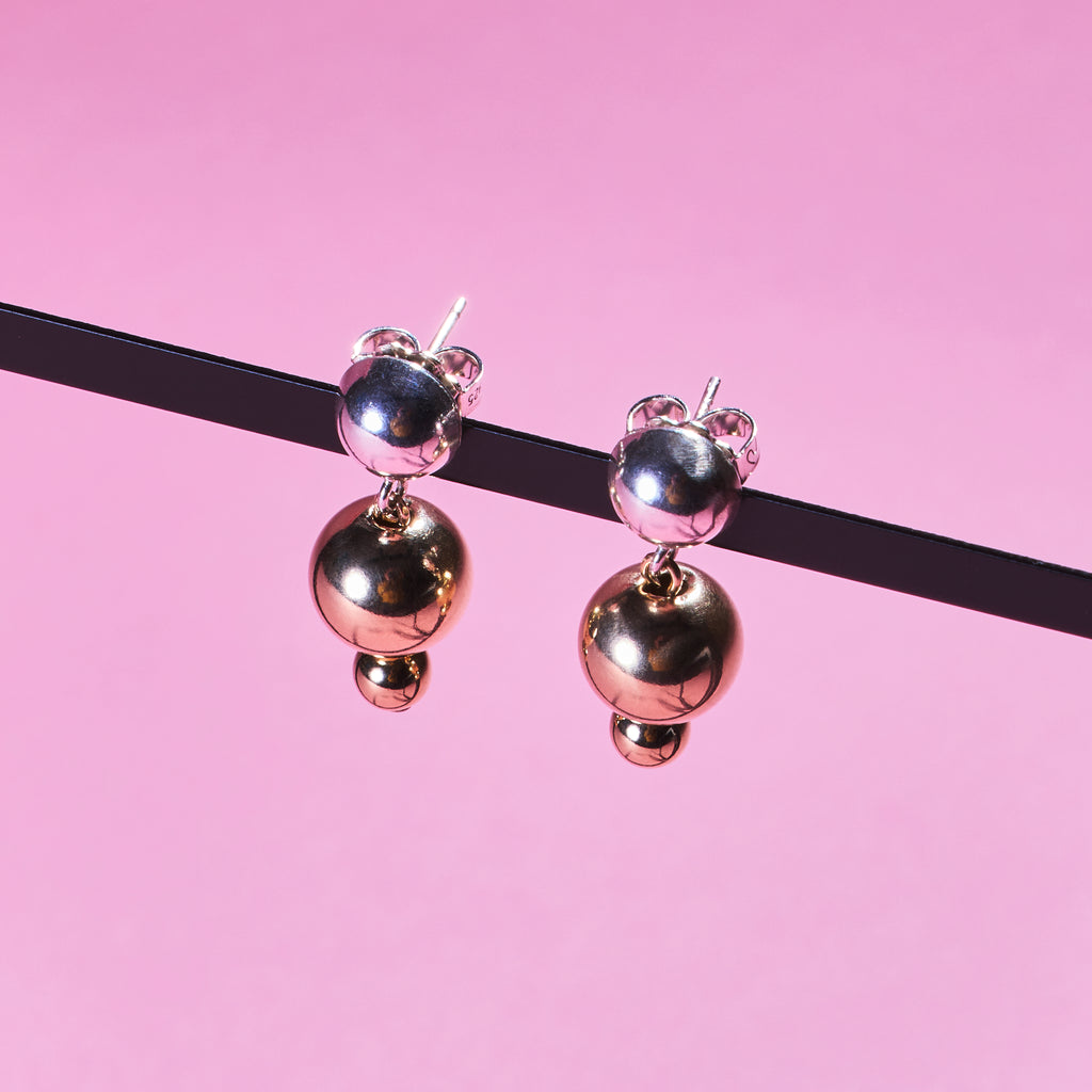 Two of Peg's Hardware's Sol earrings, hanging from a black metal frame. 