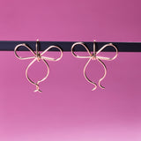 Two of Peg's Hardware's bow earrings, hanging from a black metal rod.