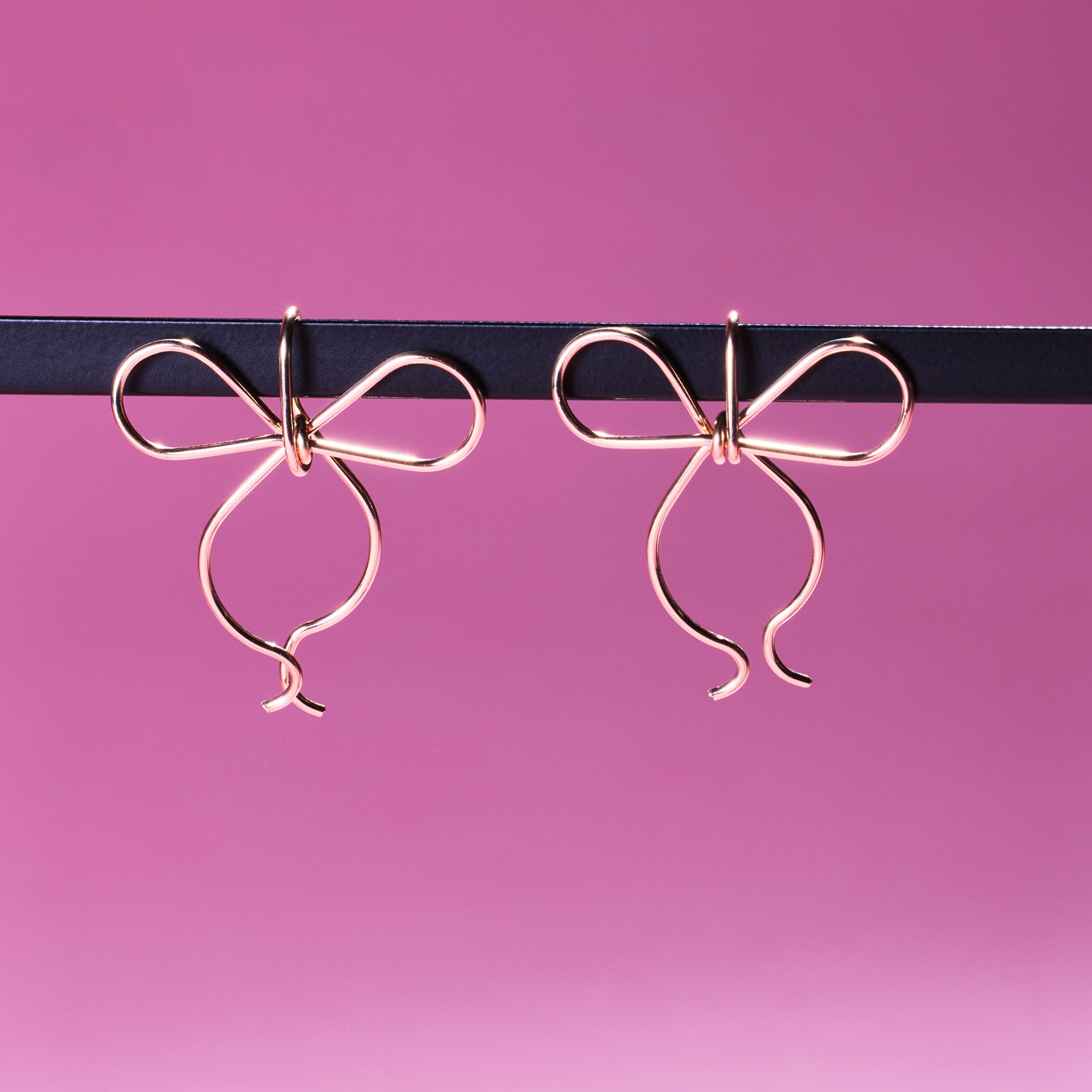 Two of Peg's Hardware's bow earrings, hanging from a black metal rod.