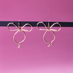 Two of Peg's Hardware's bow earrings, hanging from a black metal rod.
