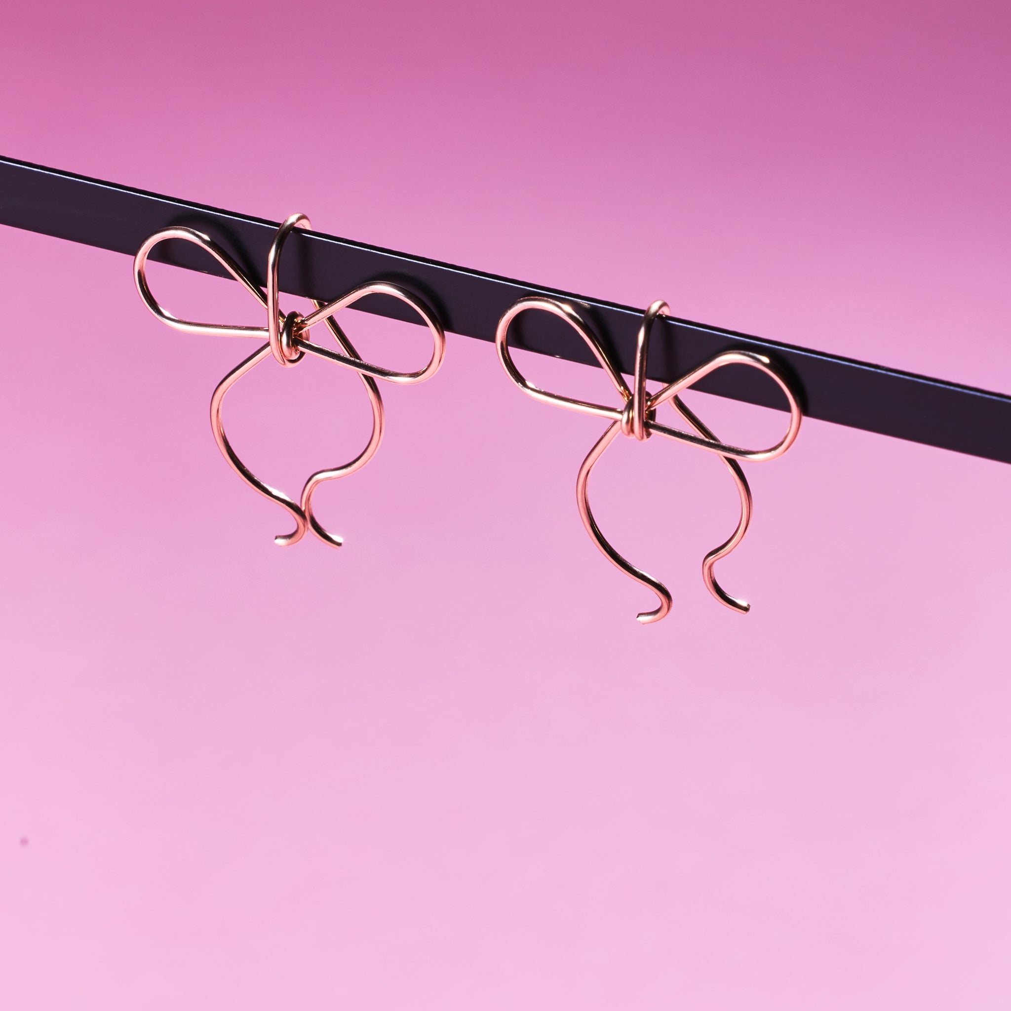 Two of Peg's Hardware's bow earrings, hanging from a black metal rod. 