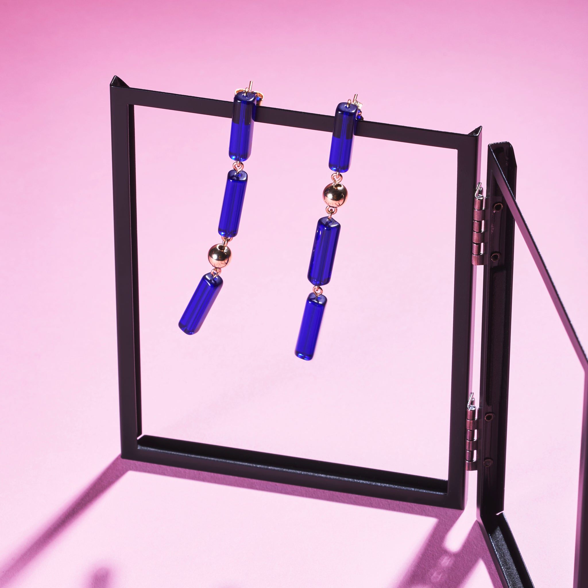 Two of Peg's Hardware's Capri earrings, hanging from a black metal frame. 