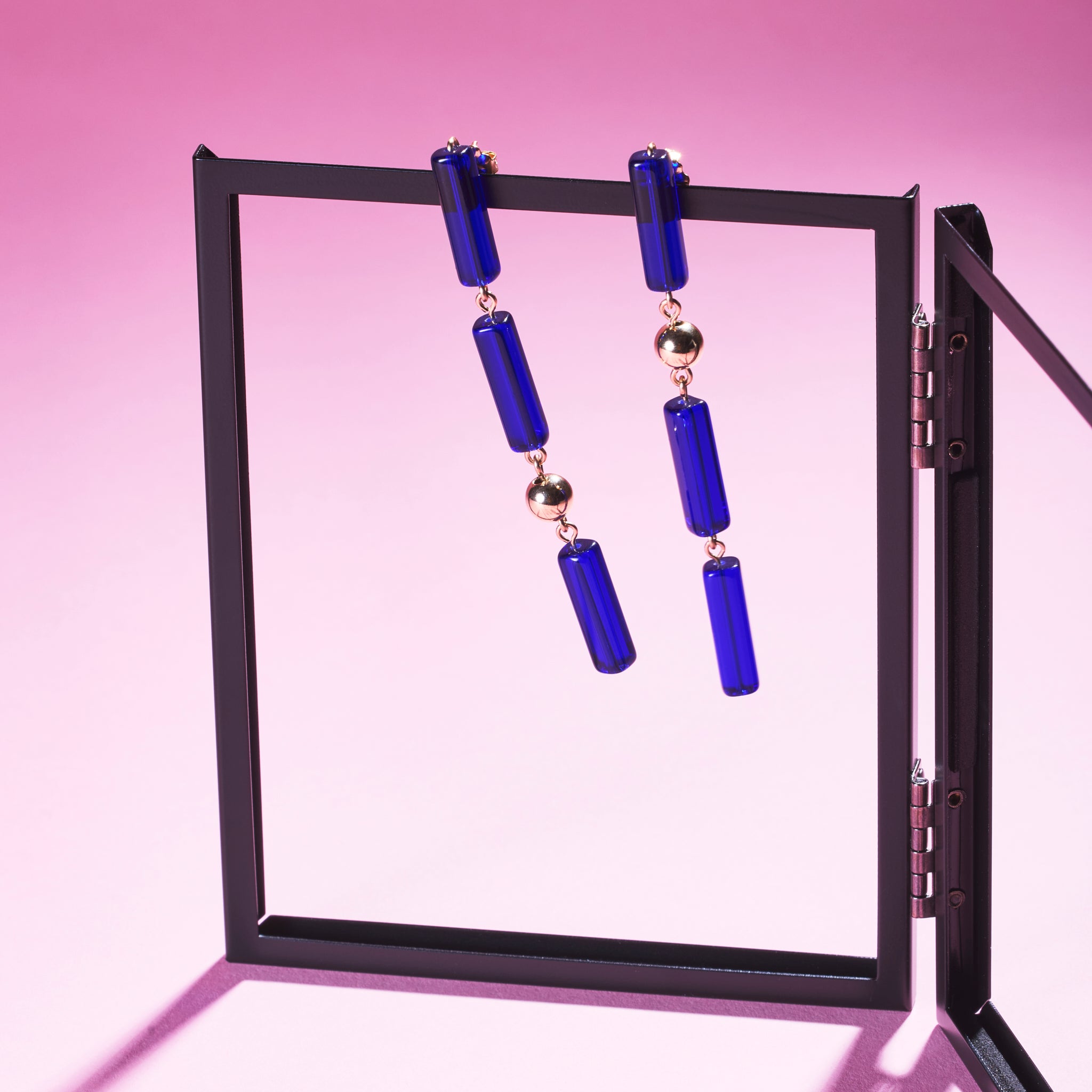 Two of Peg's Hardware's Capri earrings, hanging from a black metal frame. 