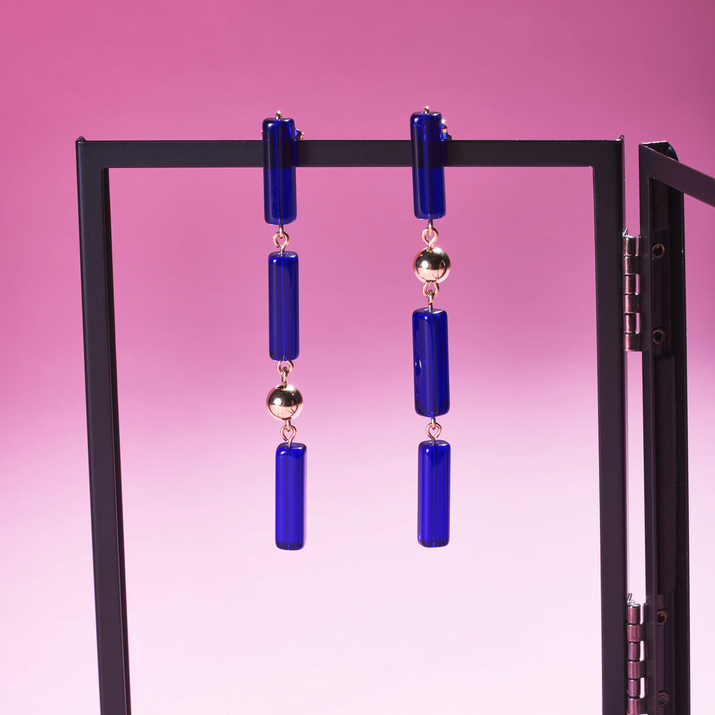 Two of Peg's Hardware's Capri earrings, hanging from a black metal frame.