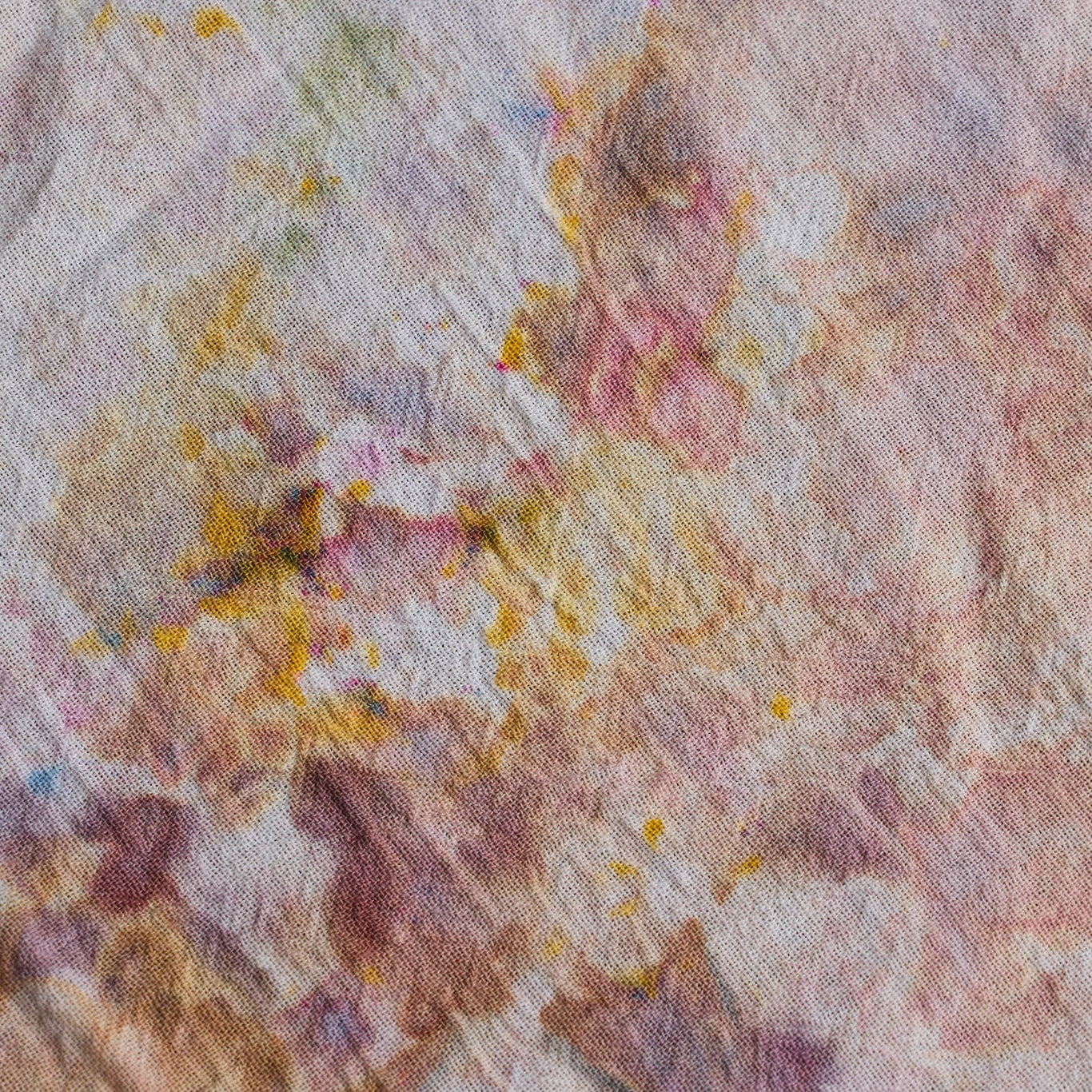 A close-up of a textured fabric with a mottled, abstract pattern in soft pastel tones including pink, beige, yellow, and purple.
