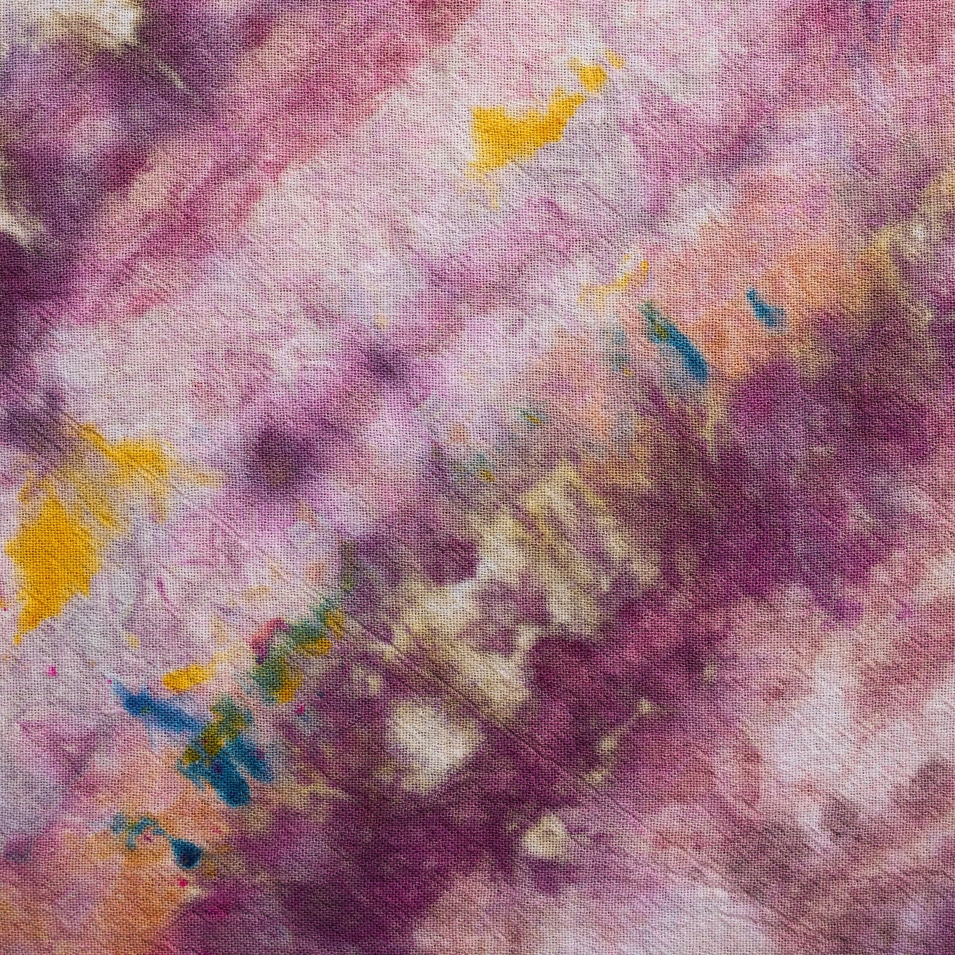 A close-up of a textured fabric with an abstract tie-dye or watercolor pattern in shades of purple, pink, peach, yellow, and blue.