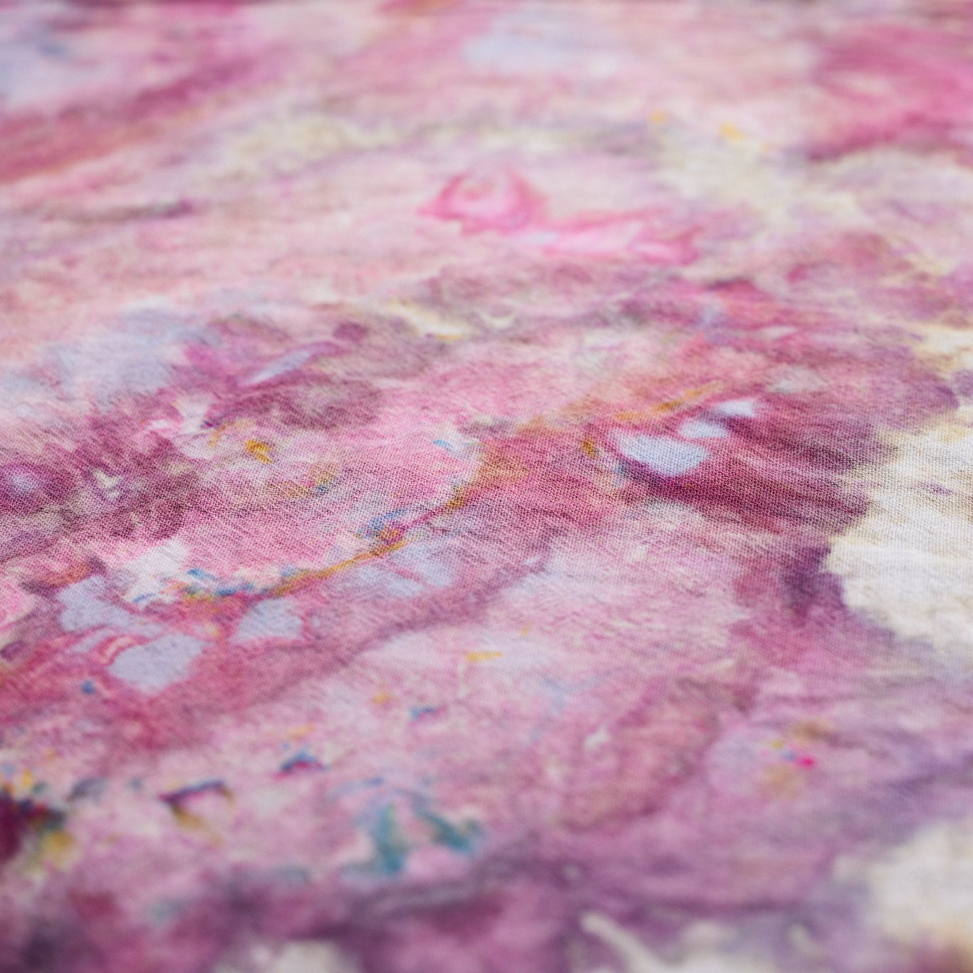 A close-up of a pink and purple marbled fabric texture with subtle beige and blue accents.