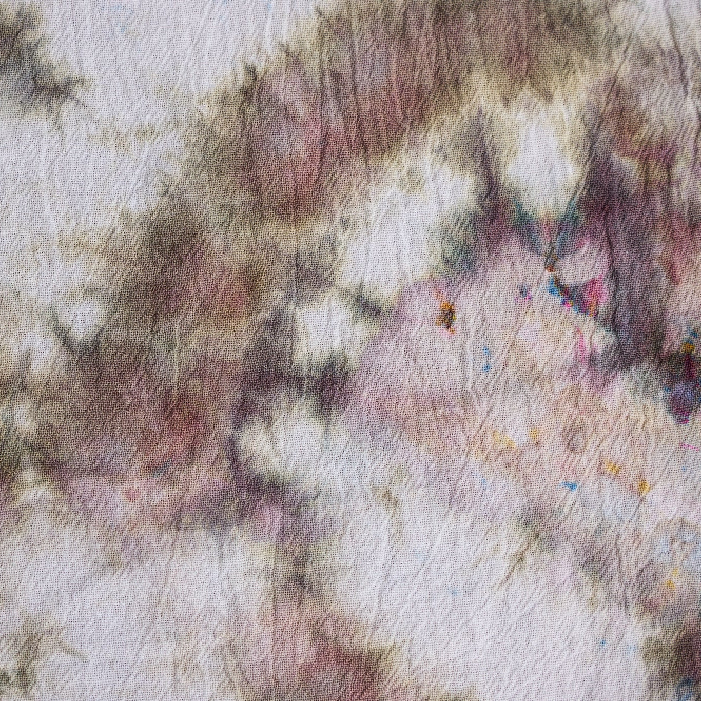 A close-up of a textured fabric with a mottled, tie-dye style pattern in dusty pink, mauve, charcoal gray, and cream.
