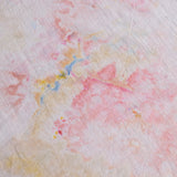 A close-up of a textured fabric with a soft watercolor-like pattern in pink, peach, pale yellow, and light blue.