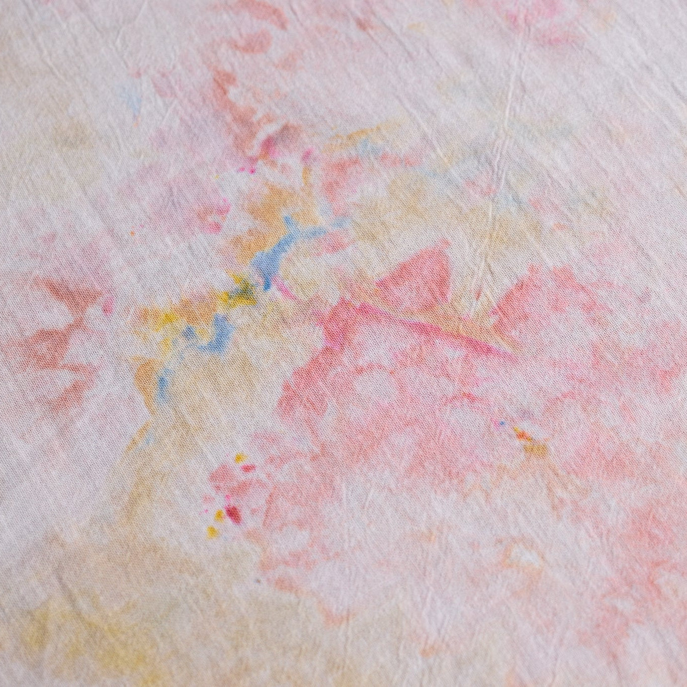 A close-up of a textured fabric with a soft watercolor-like pattern in pink, peach, pale yellow, and light blue.