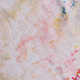 A close-up of a textured fabric with a white base and soft pastel tie-dye or watercolor-like splashes in pink, peach, yellow, blue, and green.
