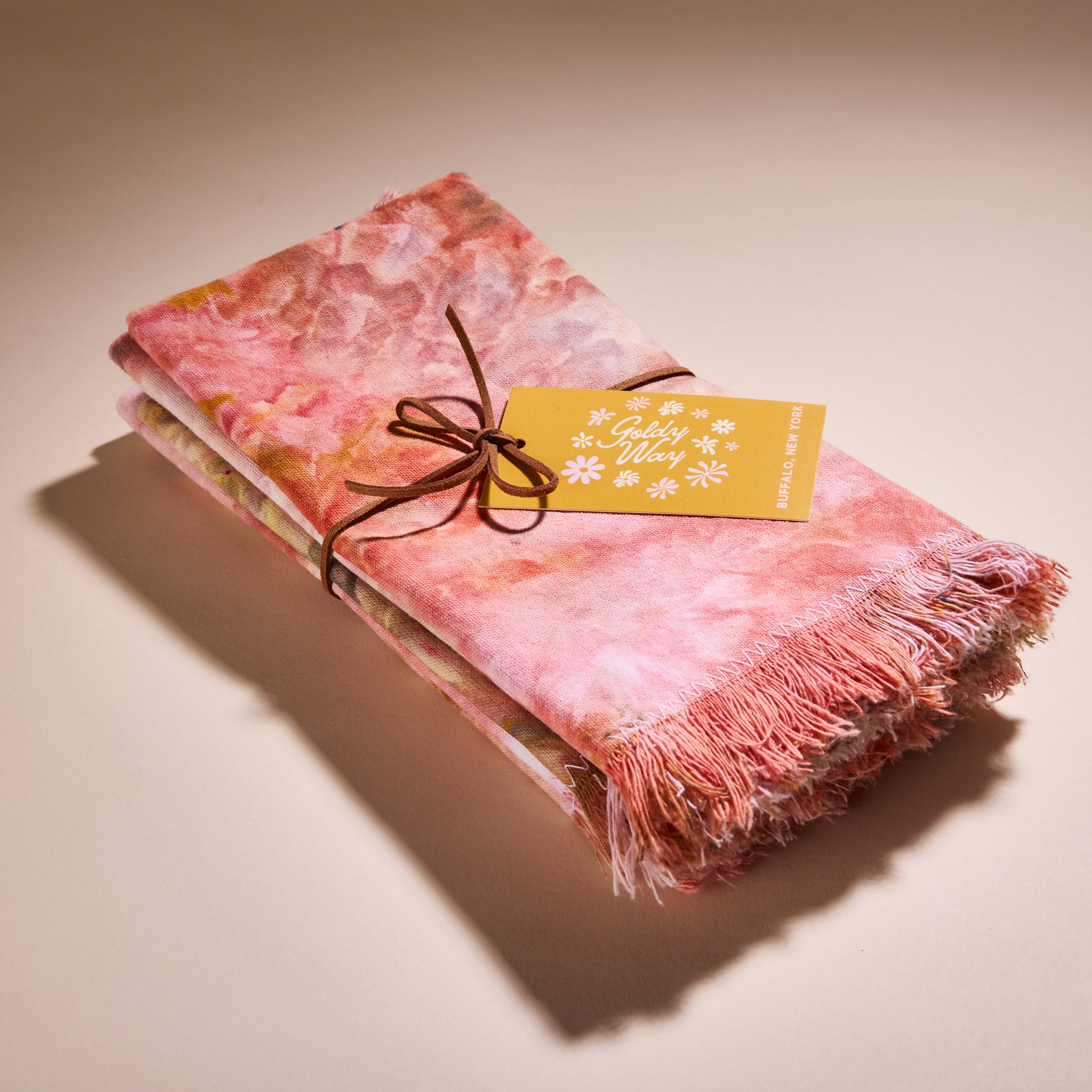 A stack of Goldy Way's hand-dyed fabric napkins, tied together with leather string and featuring a yellow Goldy Way tag.