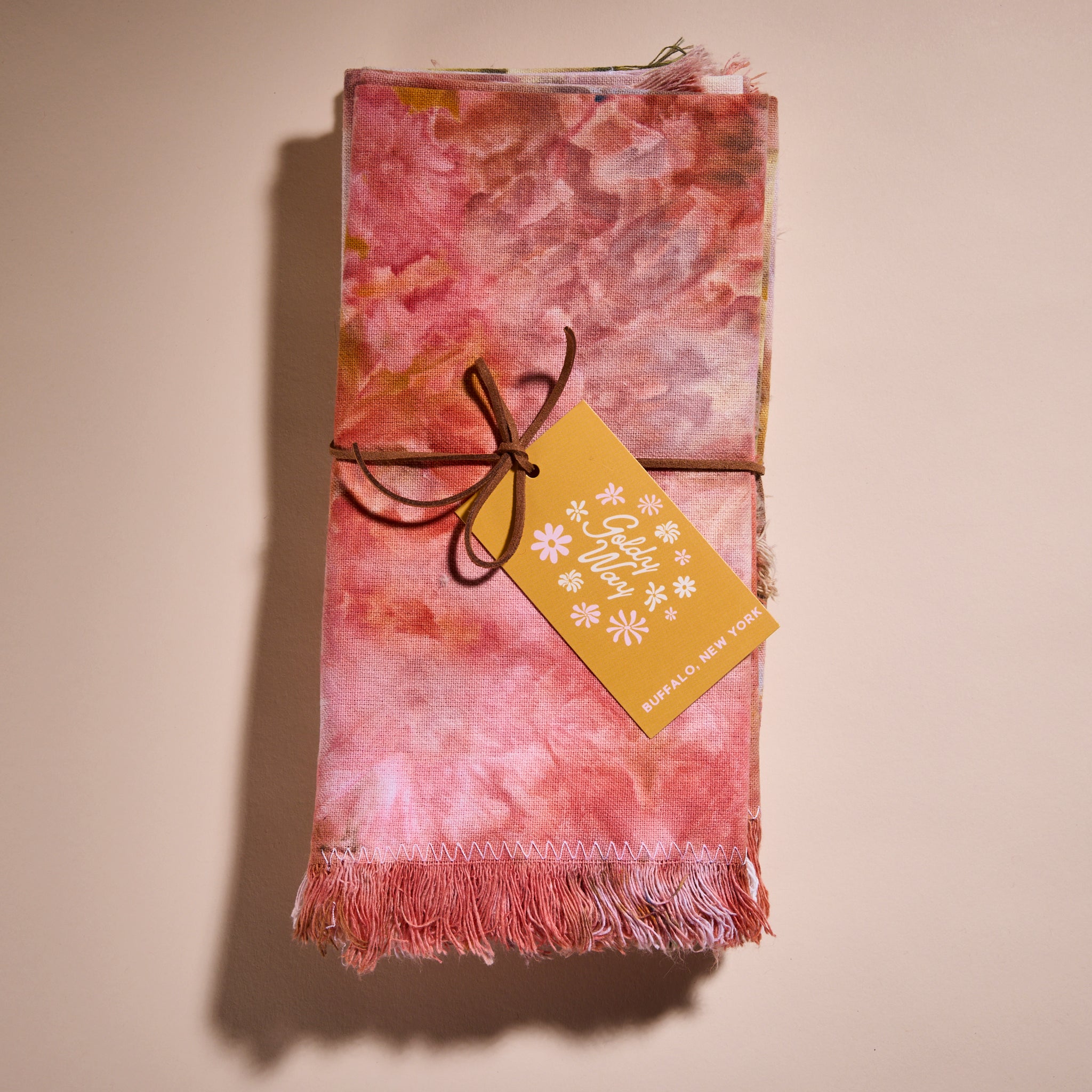 A stack of Goldy Way's hand-dyed fabric napkins, tied together with leather string and featuring a yellow Goldy Way tag. 