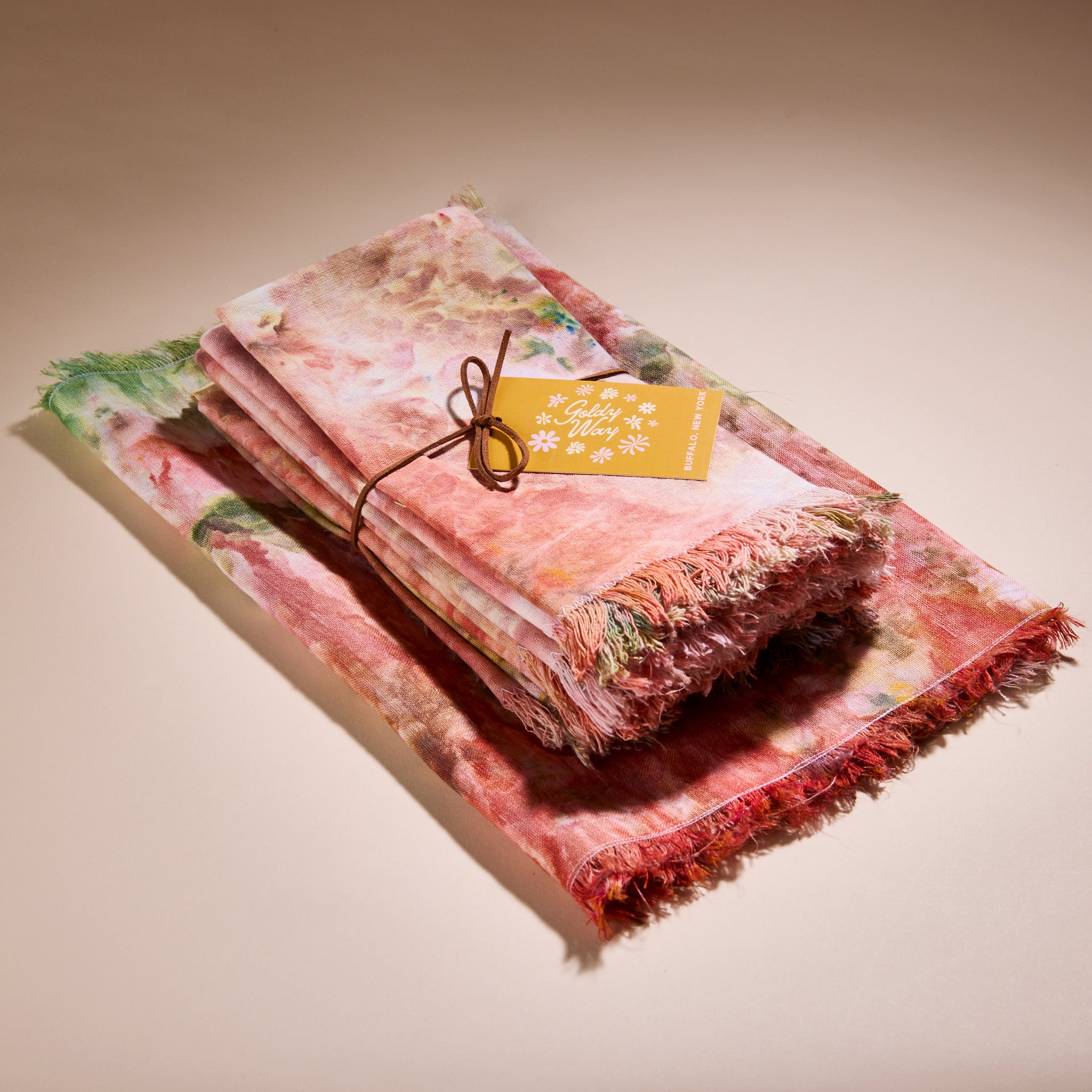 A stack of Goldy Way hand-dyed fabric napkins, on top of a hand-dyed linen table runner.