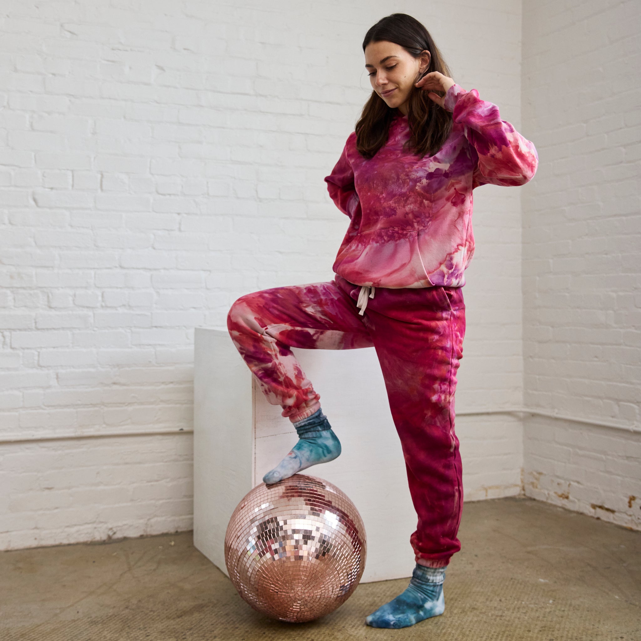 Goldy Way's ice-dyed unisex sweatsuit in the Winterberry color. The suit is worn by a model who is also wearing Goldy Way's hand-dyed crew socks in the Lake Effect color.
