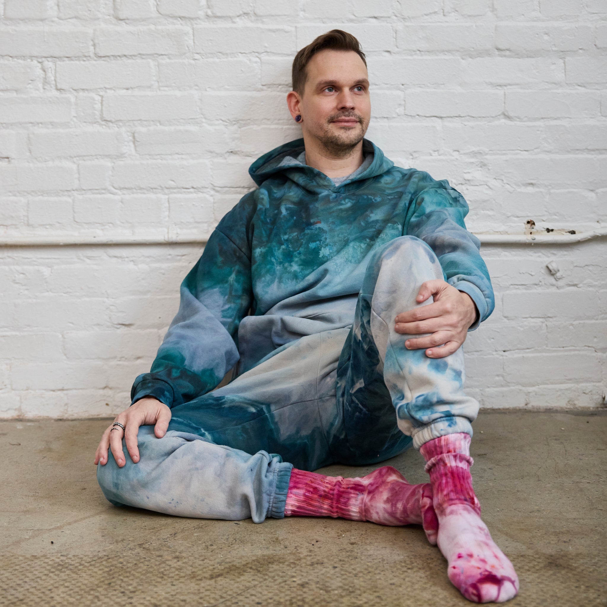 Goldy Way's ice-dyed unisex sweatsuit in the Lake Effect color. The suit is worn by a model who is also wearing Goldy Way's hand-dyed crew socks in the Winterberry color.