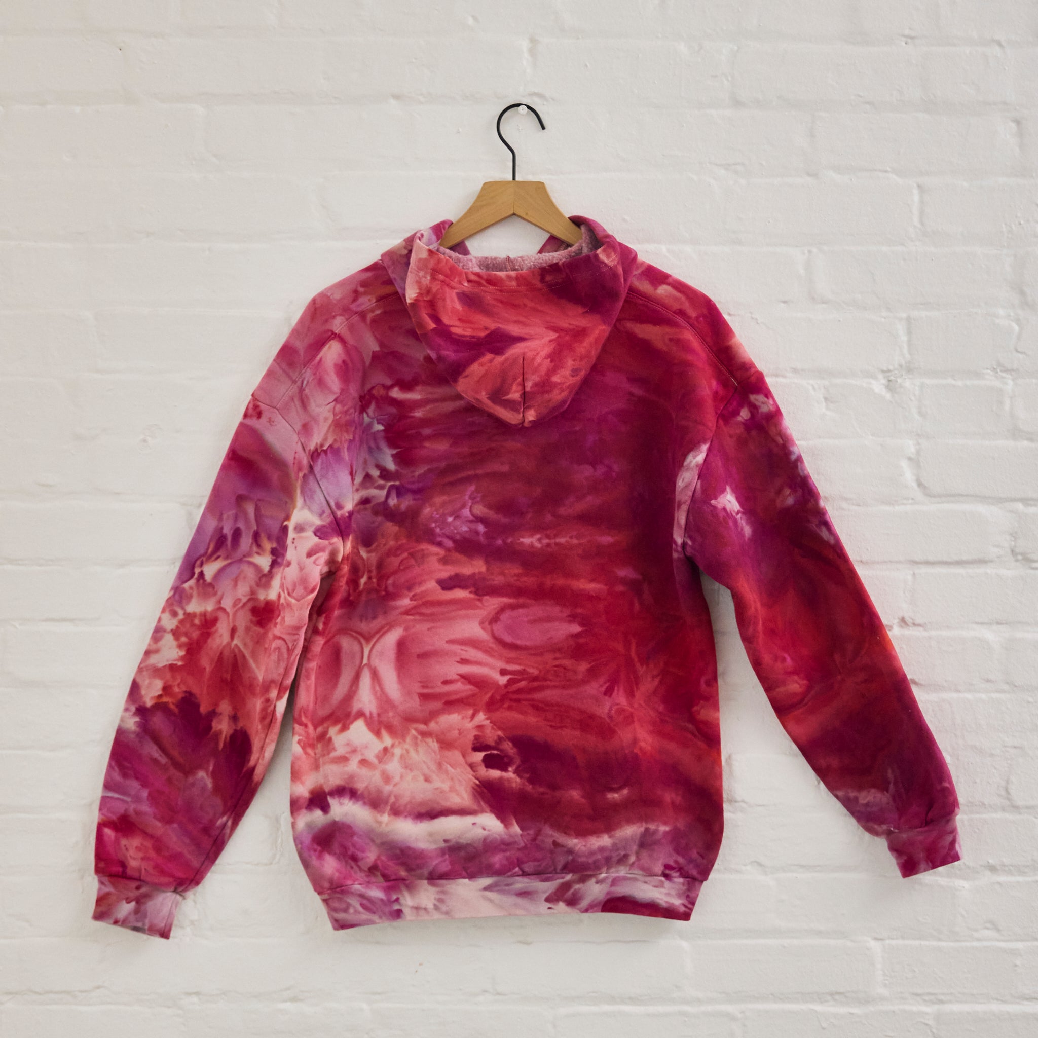 the back of Goldy Way's ice-dyed unisex sweatshirt, with the Winterberry color displayed on a hanger.