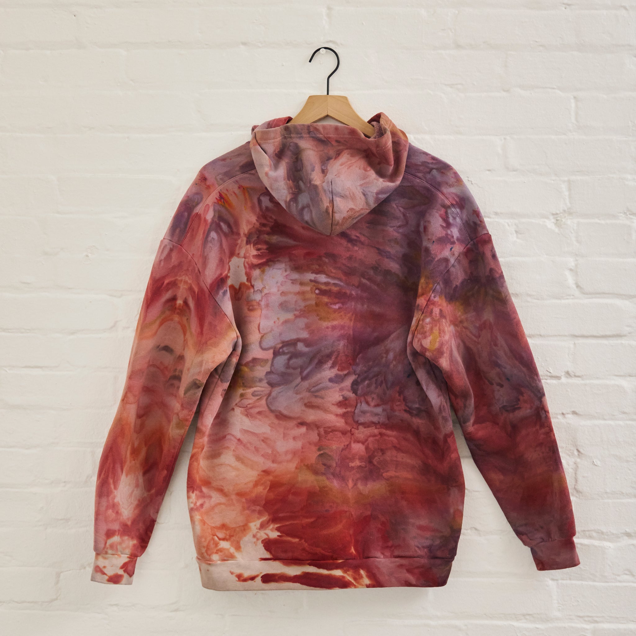 the back of Goldy Way's ice-dyed unisex sweatshirt, with the Solstice color displayed on a hanger.