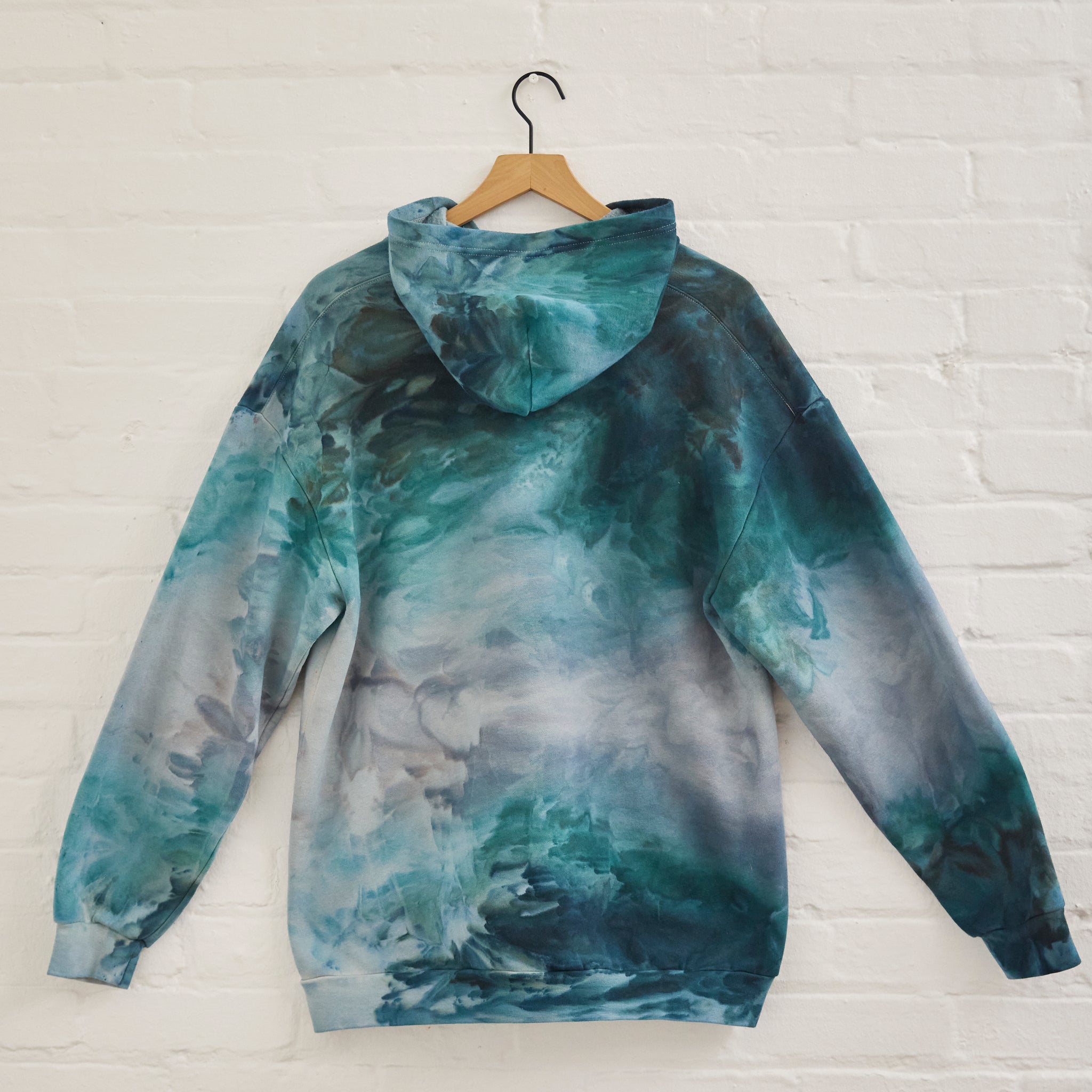 the back of Goldy Way's ice-dyed unisex sweatshirt, with the Lake Effect color displayed on a hanger.
