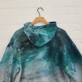 the back of Goldy Way's ice-dyed unisex sweatshirt, with the Lake Effect color displayed on a hanger.