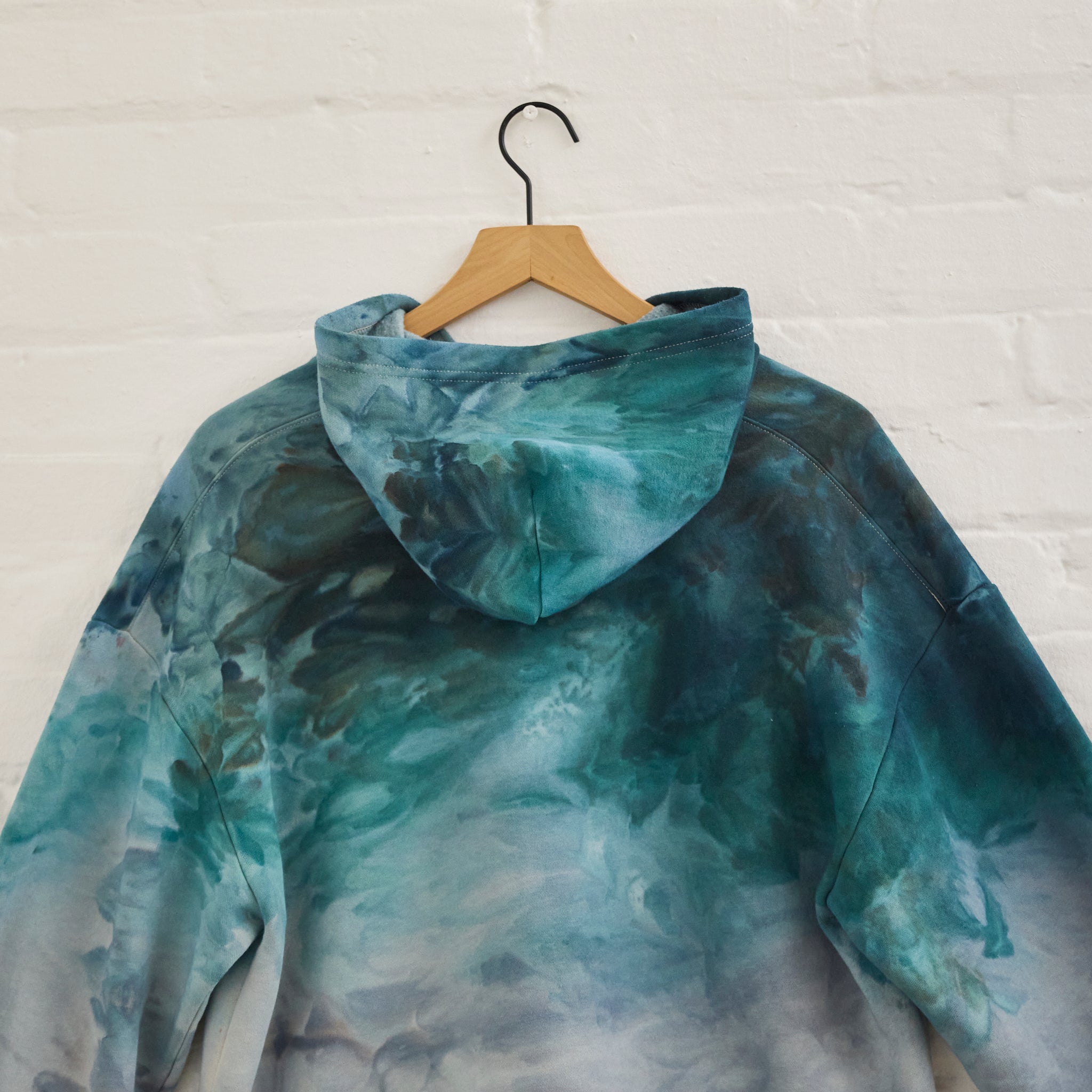 the back of Goldy Way's ice-dyed unisex sweatshirt, with the Lake Effect color displayed on a hanger.