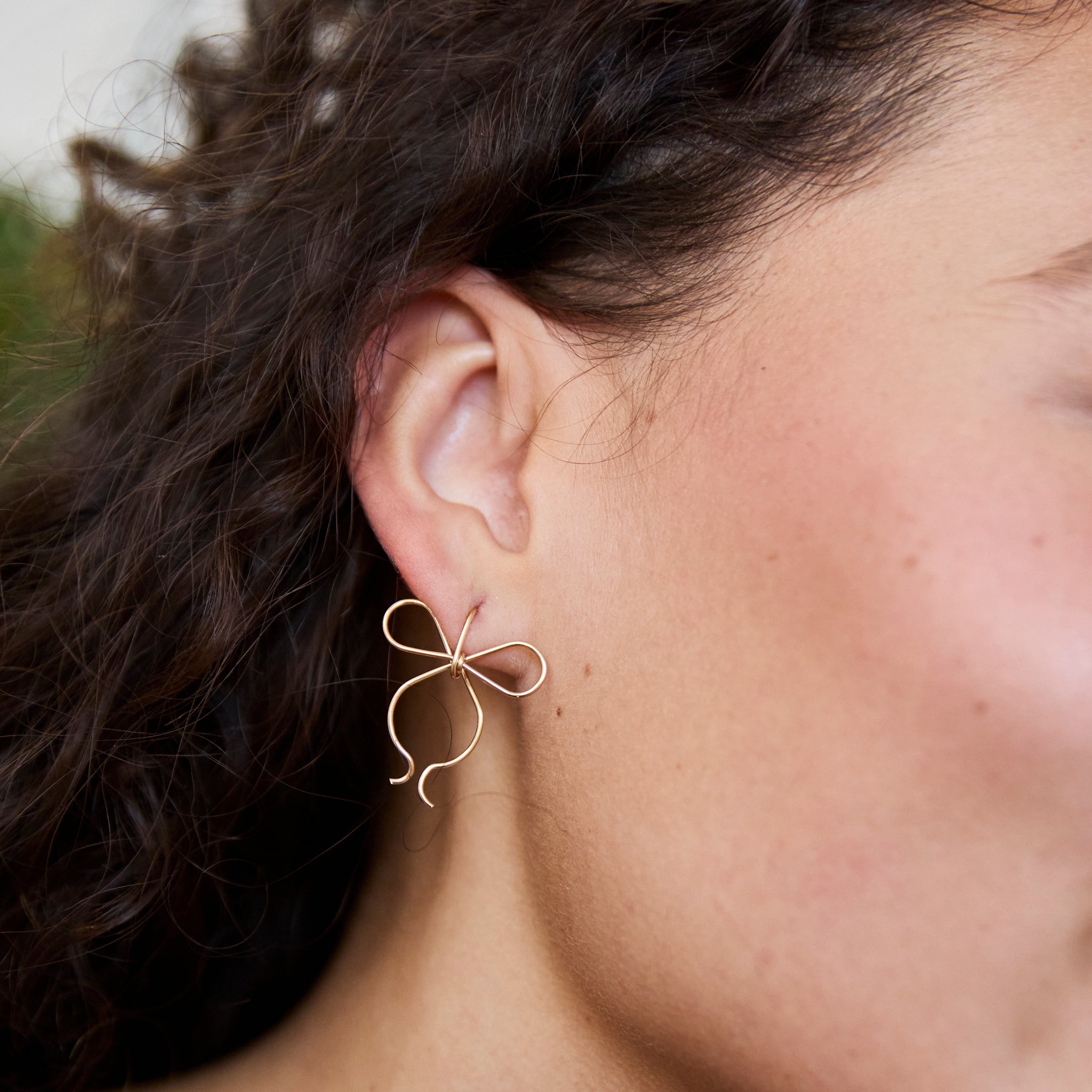 One of Peg's Hardware's bow earrings, hanging from a model's ear. 
