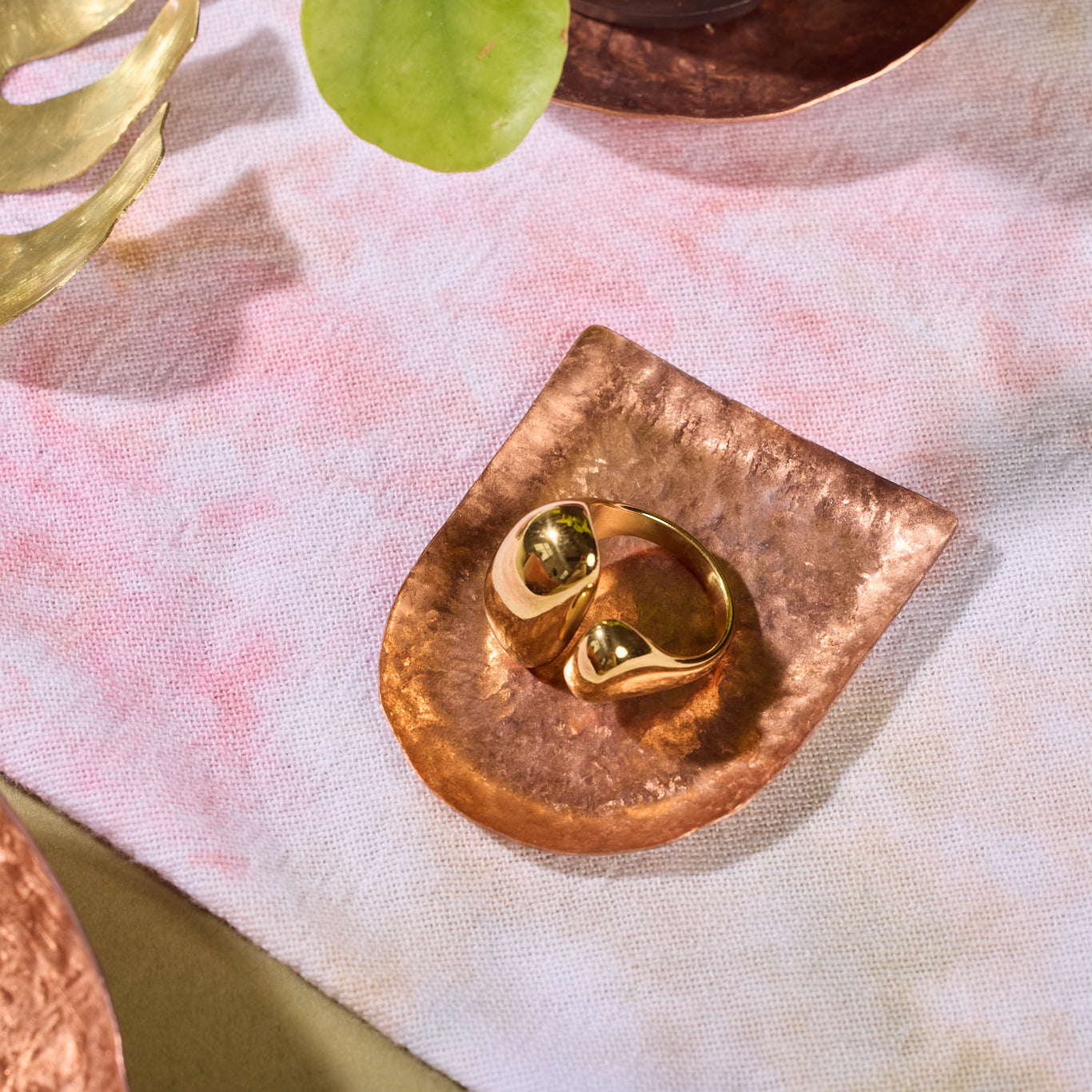 An earring sits on a semicircular hammered bronze tray.