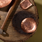Hammered brass trinket trays sit on a stump. There is a hammer with a wooden handle for working brass next to the trays.