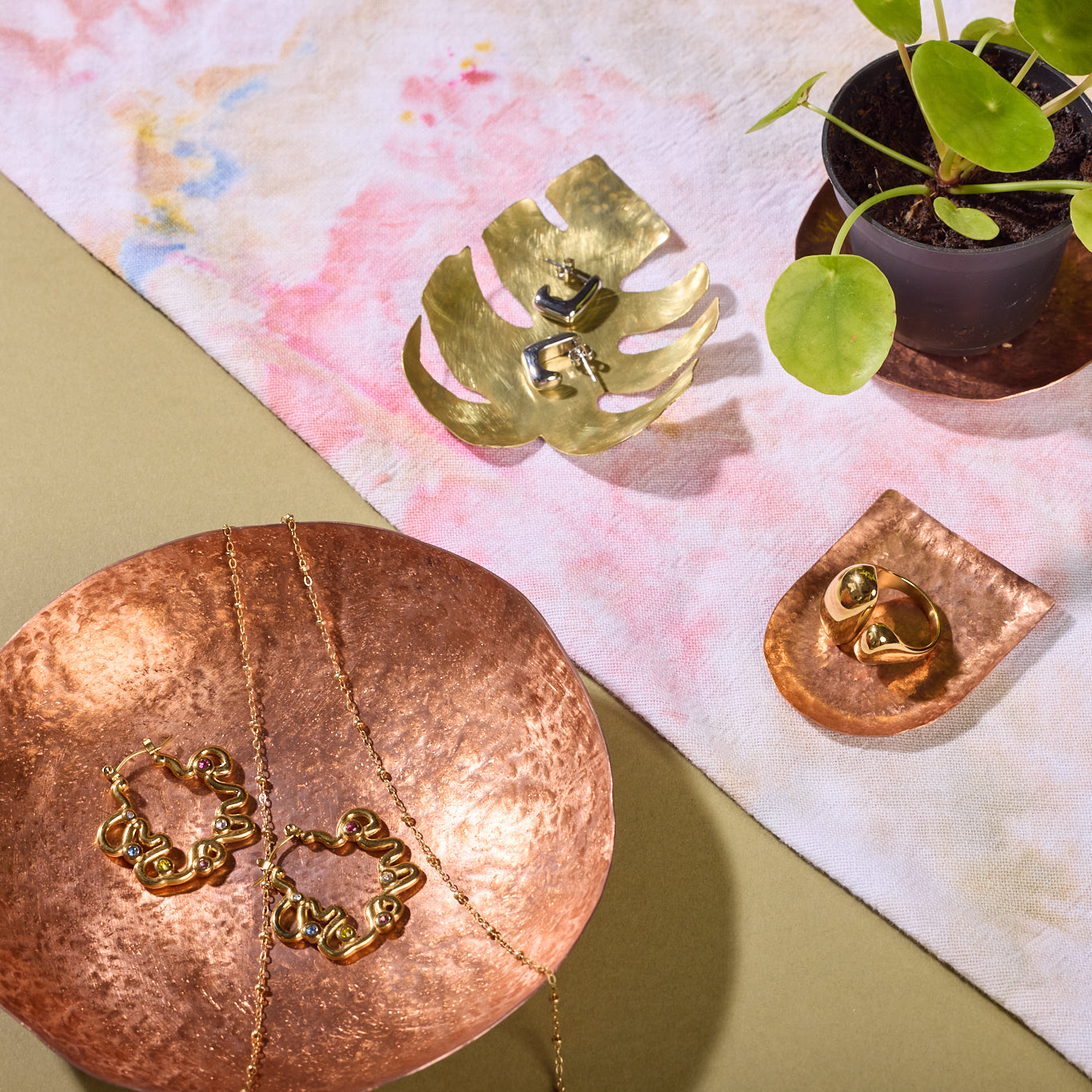 Four bonze trays sit on a counter holding jewlery and plants.