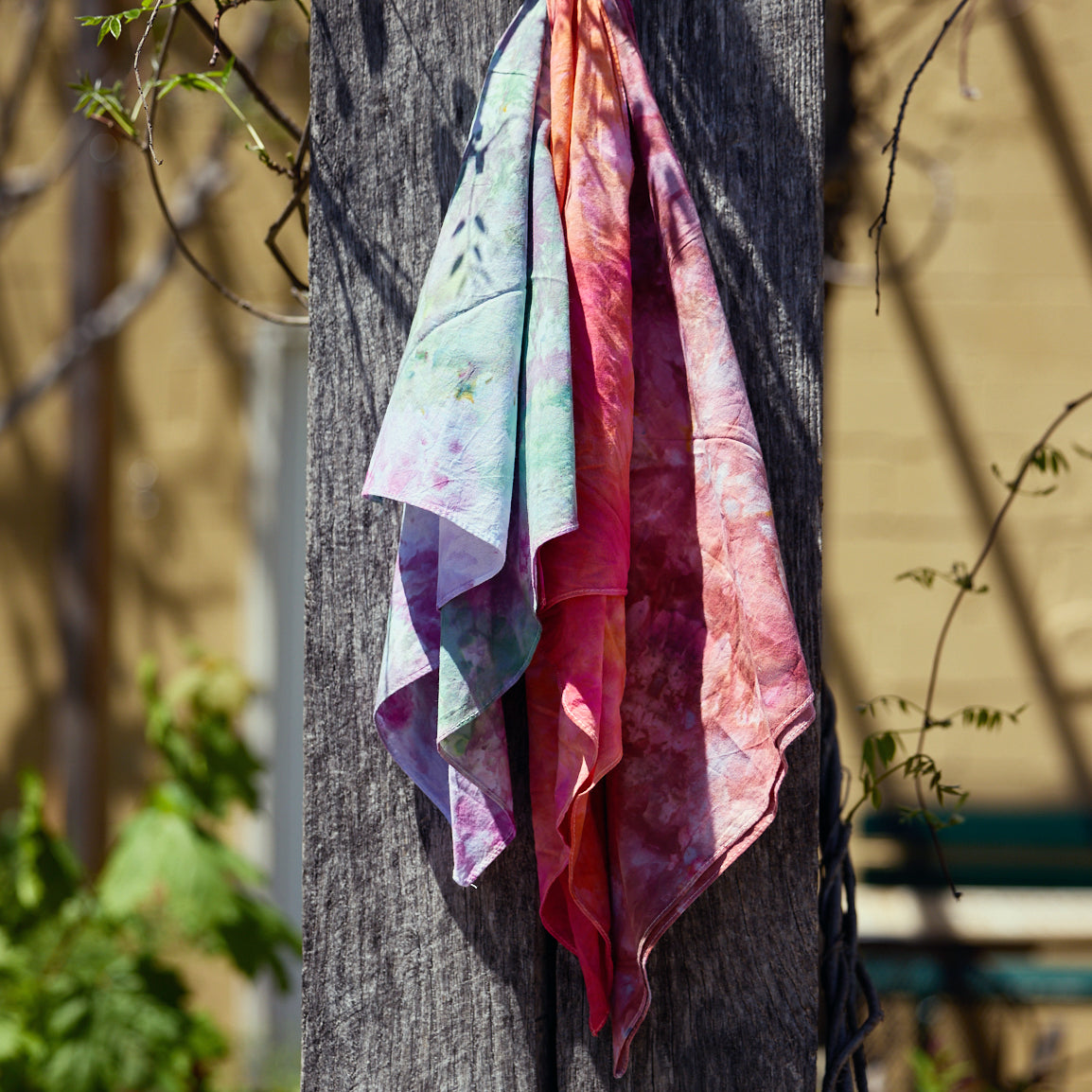 Ice-dyed bandanas hang on a post.
