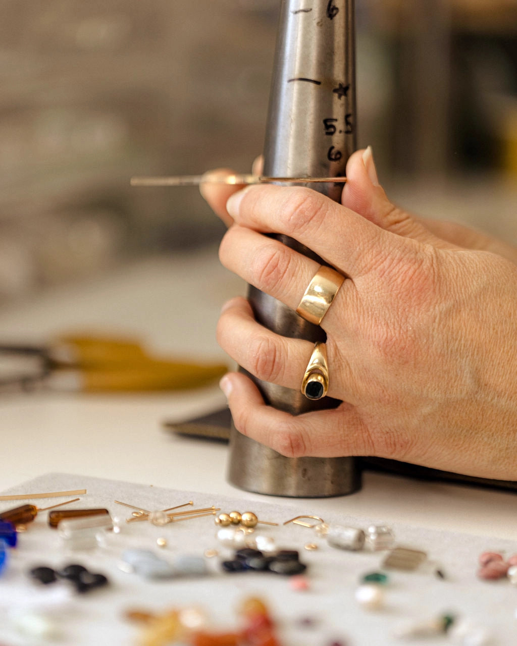Hand holding a metal tool over a jewelry-making setup with beads and tools on a table.
